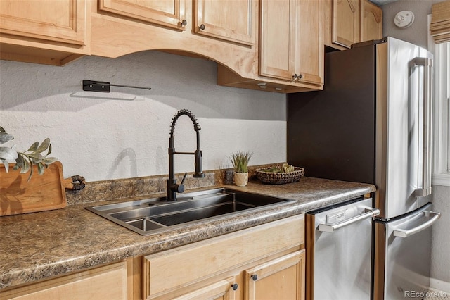 kitchen with light brown cabinets, appliances with stainless steel finishes, dark countertops, and a sink