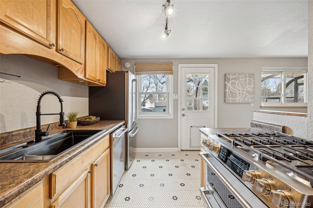 kitchen with a textured ceiling, a sink, baseboards, appliances with stainless steel finishes, and light floors