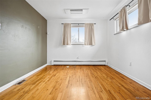 empty room featuring baseboards, visible vents, baseboard heating, and wood finished floors