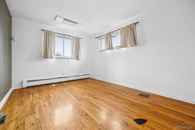 spare room with hardwood / wood-style flooring, a baseboard radiator, visible vents, and baseboards