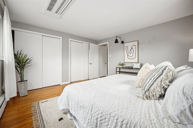 bedroom featuring wood finished floors, visible vents, and multiple closets