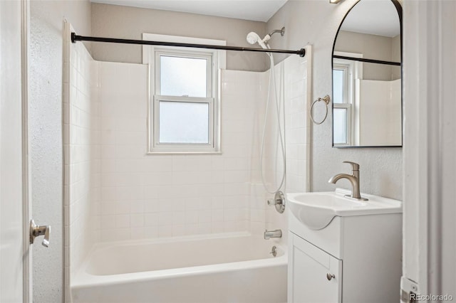 bathroom with a textured wall, shower / tub combination, vanity, and a healthy amount of sunlight