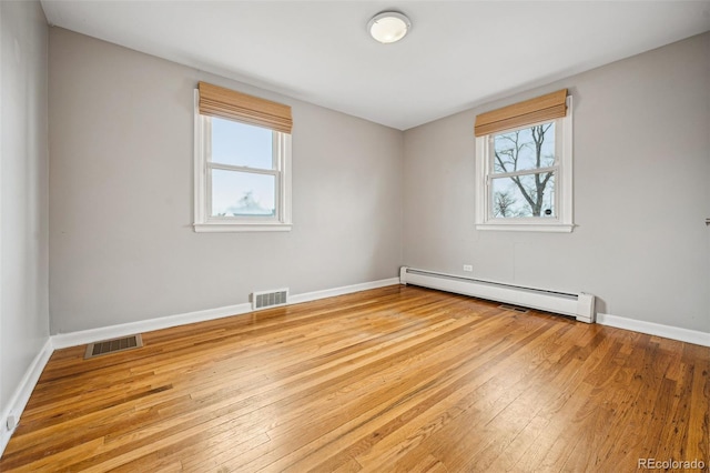 unfurnished room featuring hardwood / wood-style flooring, visible vents, and a baseboard heating unit