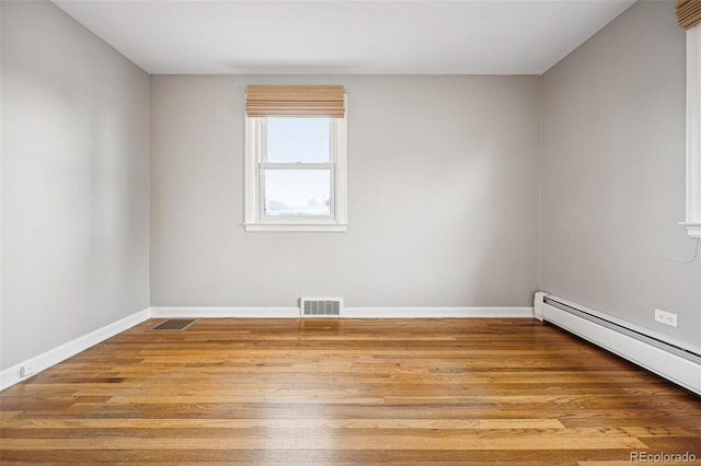 empty room with a baseboard heating unit, light wood finished floors, visible vents, and baseboards