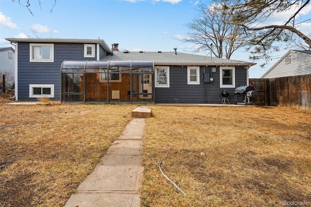 rear view of house with a patio, a chimney, a lawn, a sunroom, and fence