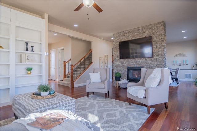 living room with ceiling fan, dark hardwood / wood-style flooring, a stone fireplace, and built in features