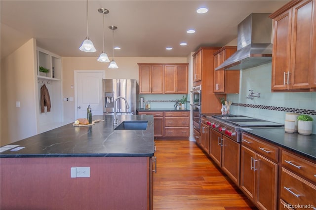 kitchen with wall chimney exhaust hood, sink, a kitchen island with sink, and appliances with stainless steel finishes