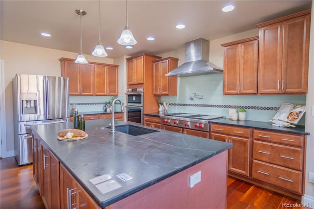 kitchen featuring wall chimney range hood, sink, decorative backsplash, an island with sink, and appliances with stainless steel finishes