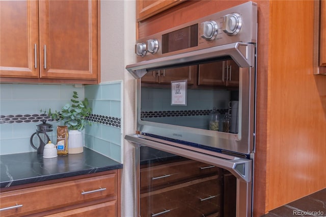 kitchen with dark stone countertops, decorative backsplash, and stainless steel double oven