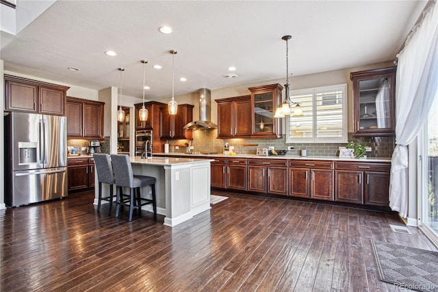 kitchen featuring dark wood-type flooring, light countertops, appliances with stainless steel finishes, wall chimney exhaust hood, and tasteful backsplash