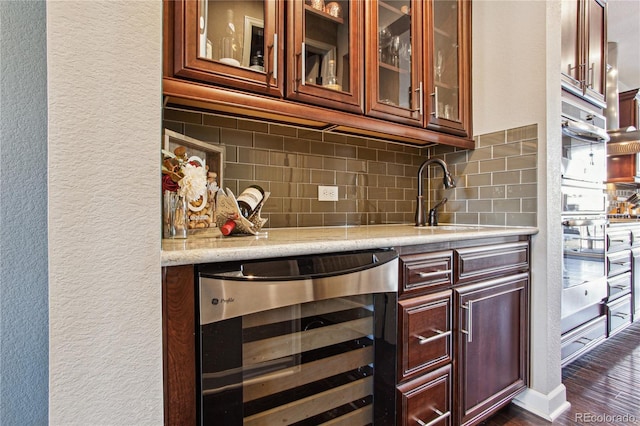 bar with beverage cooler, a textured wall, dark wood-type flooring, a sink, and backsplash