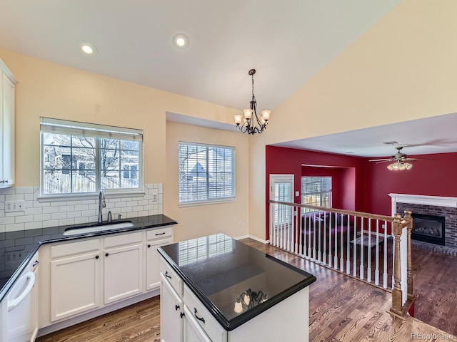 kitchen with white dishwasher, wood finished floors, a sink, white cabinets, and dark countertops