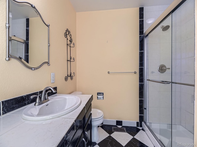 bathroom featuring toilet, a stall shower, vanity, baseboards, and tile patterned floors