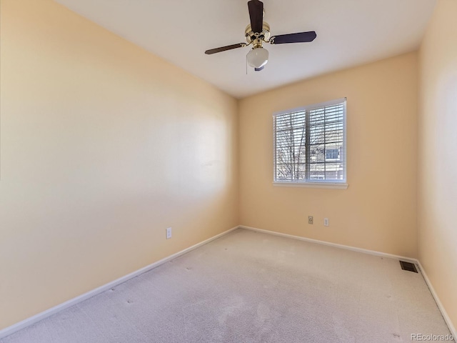 carpeted spare room with visible vents, baseboards, and ceiling fan