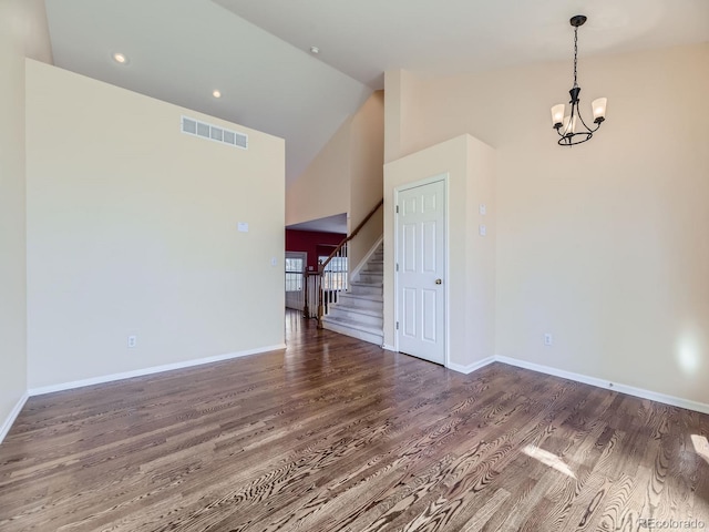 empty room with a notable chandelier, visible vents, vaulted ceiling, wood finished floors, and stairs