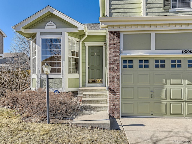 view of exterior entry featuring a garage, driveway, and brick siding