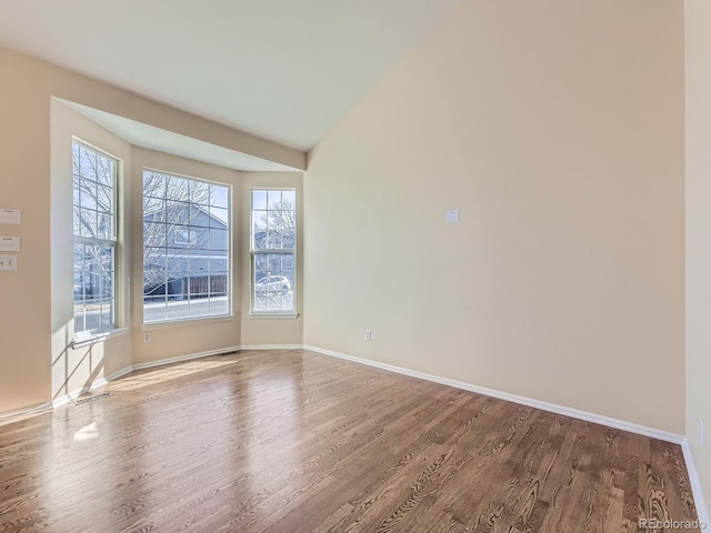 unfurnished room featuring vaulted ceiling, wood finished floors, and baseboards