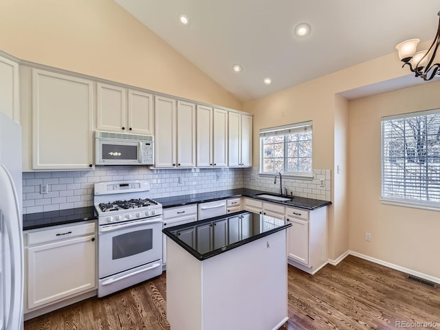 kitchen featuring dark countertops, visible vents, white cabinetry, a sink, and white appliances