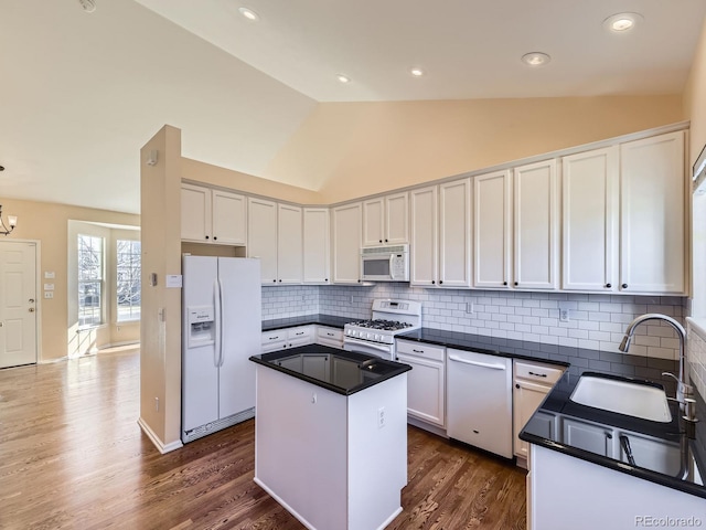 kitchen with white appliances, dark wood finished floors, dark countertops, white cabinetry, and a sink