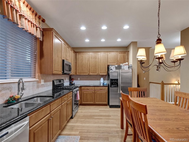 kitchen with sink, appliances with stainless steel finishes, dark stone countertops, hanging light fixtures, and light wood-type flooring