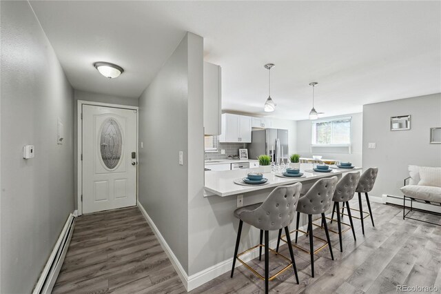 1390 Everett Ct Unit 105, Lakewood, CO 80215 - kitchen with stainless steel fridge, baseboard heating, light wood-style flooring, white cabinets, and a kitchen breakfast bar