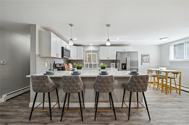 1390 Everett Ct Unit 105, Lakewood, CO 80215 - kitchen with appliances with stainless steel finishes, baseboard heating, a breakfast bar area, decorative backsplash, and a peninsula