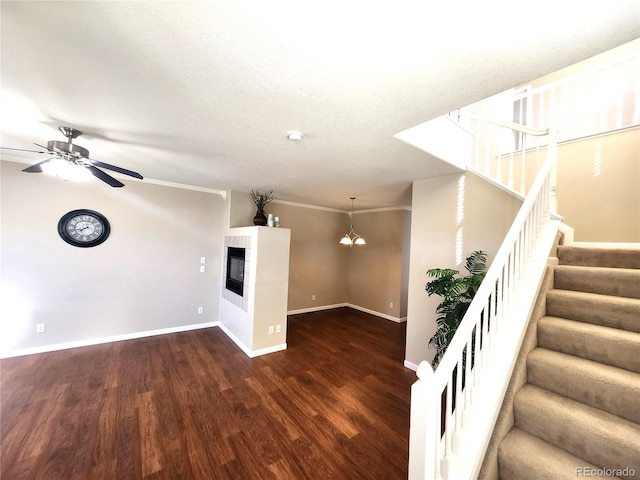 unfurnished living room featuring ceiling fan with notable chandelier, ornamental molding, and dark wood-type flooring