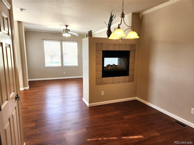 unfurnished room with dark wood-style flooring, visible vents, a ceiling fan, crown molding, and a fireplace