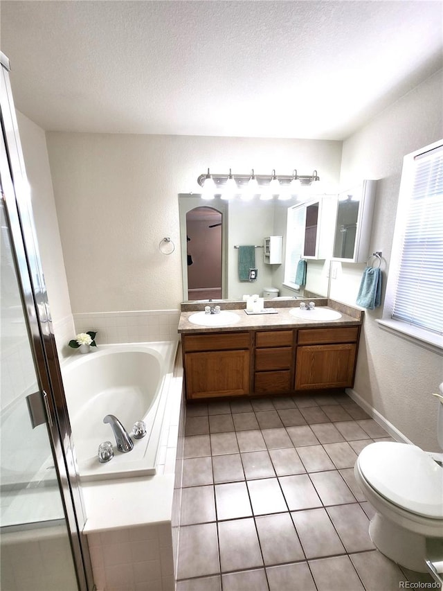 bathroom with tile patterned floors, tiled tub, a textured ceiling, toilet, and vanity