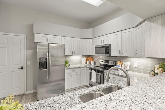 6868 Los Reyes Cir, Colorado Springs, CO 80918 - kitchen featuring appliances with stainless steel finishes, a sink, light stone countertops, backsplash, and light wood finished floors