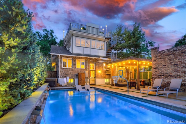 pool at dusk featuring a patio and pool water feature