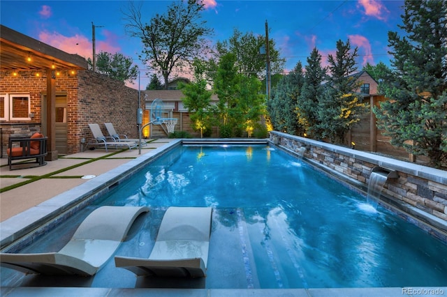 pool at dusk featuring pool water feature and a patio