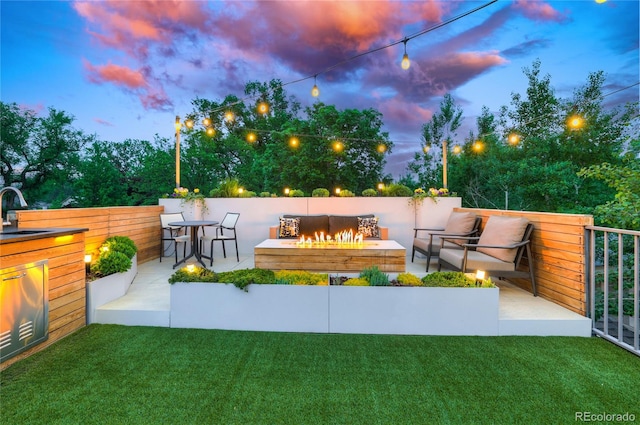 patio terrace at dusk featuring sink, a fire pit, and a lawn