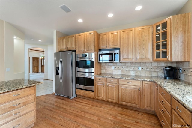 6323 S Sicily Way, Aurora, CO 80016 - kitchen featuring stainless steel appliances, arched walkways, backsplash, light wood-type flooring, and glass insert cabinets