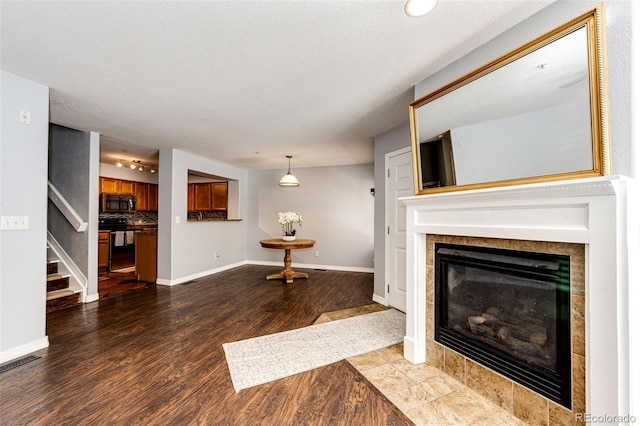 unfurnished living room with visible vents, a tiled fireplace, wood finished floors, stairway, and baseboards