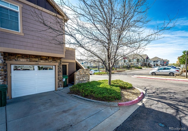 view of property exterior with an attached garage, a residential view, driveway, and stone siding