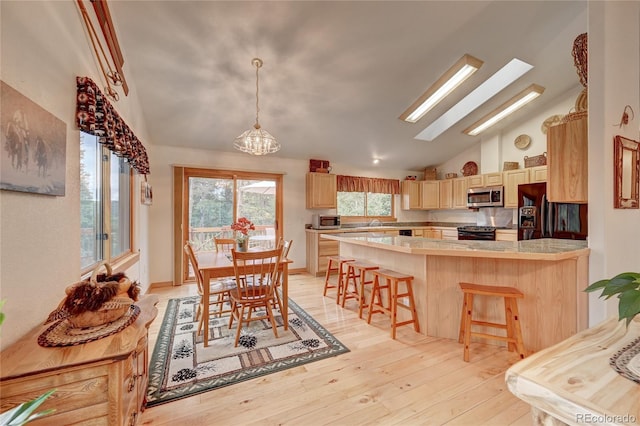 kitchen featuring a skylight, high vaulted ceiling, light hardwood / wood-style floors, a breakfast bar area, and black appliances