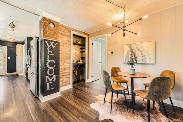 dining room with a chandelier, dark wood finished floors, baseboards, and wood walls
