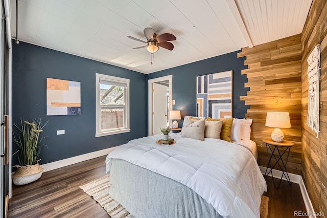 bedroom featuring wood walls, wood finished floors, baseboards, an accent wall, and a ceiling fan