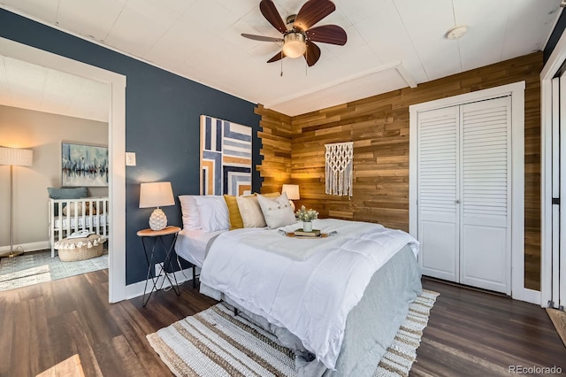 bedroom featuring wooden walls, dark wood-style flooring, baseboards, a closet, and a ceiling fan