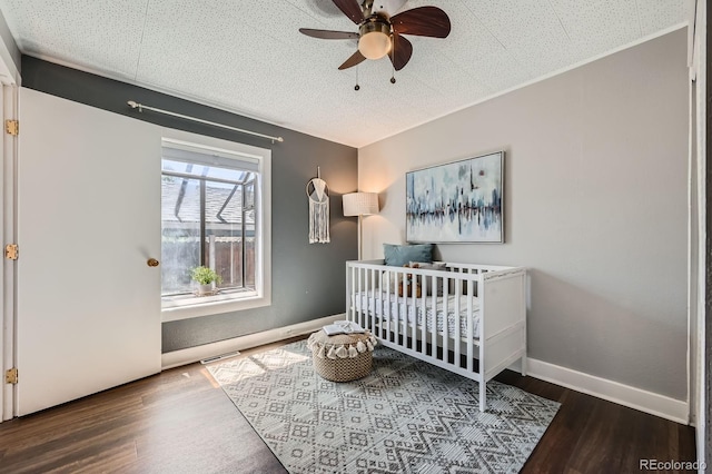 bedroom with wood finished floors, a crib, a ceiling fan, and baseboards