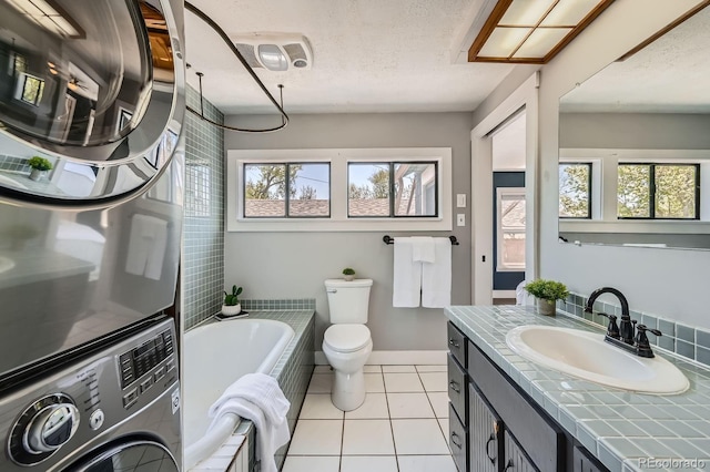 bathroom with stacked washer / drying machine, a tub to relax in, toilet, tile patterned floors, and vanity