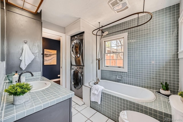 bathroom with stacked washer and clothes dryer, tile patterned floors, vanity, and tiled shower / bath