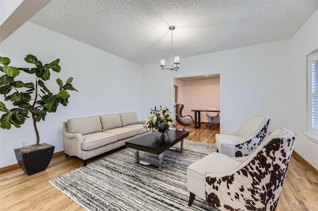 living room featuring baseboards, light wood-style flooring, a chandelier, and a textured ceiling