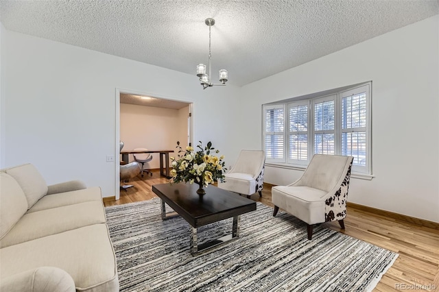 living area featuring a notable chandelier, a textured ceiling, baseboards, and wood finished floors