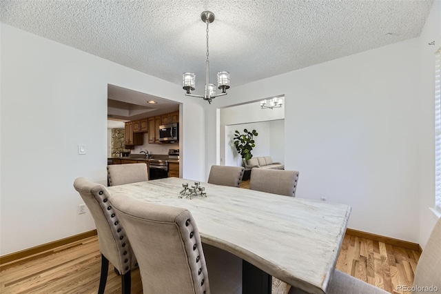 dining space with a tray ceiling, light wood finished floors, an inviting chandelier, a textured ceiling, and baseboards