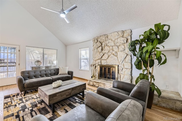 living room with ceiling fan, wood finished floors, a textured ceiling, a stone fireplace, and high vaulted ceiling