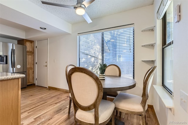 dining area featuring a ceiling fan, light wood-style flooring, baseboards, and a textured ceiling