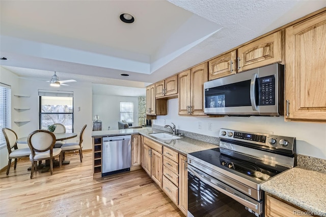 kitchen featuring a raised ceiling, appliances with stainless steel finishes, a sink, light wood-type flooring, and a peninsula