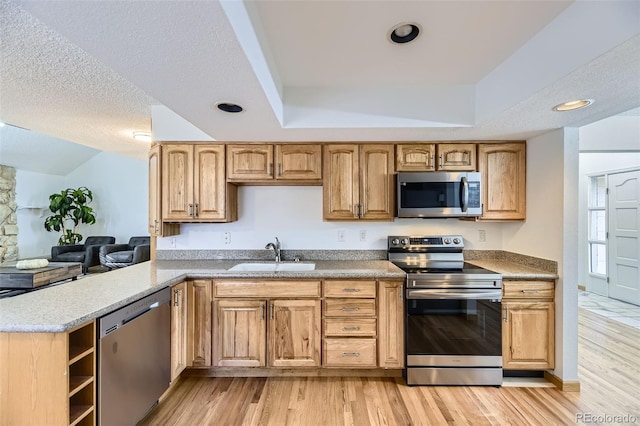 kitchen with light wood finished floors, appliances with stainless steel finishes, a textured ceiling, and a sink